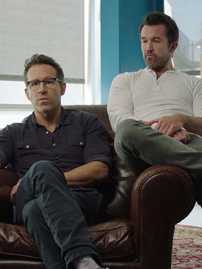 Ryan Reynolds and Rob McElhenny sitting on a brown leather chair