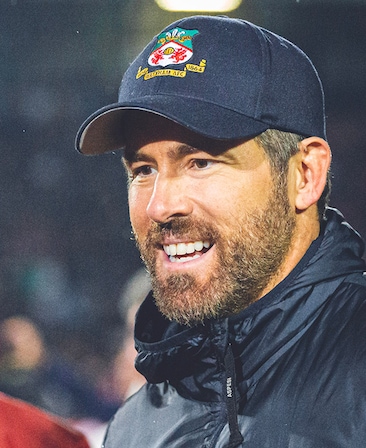 Ryan Reynolds Headshot wearing a cap with the Wrexham logo and a puffer jacket
