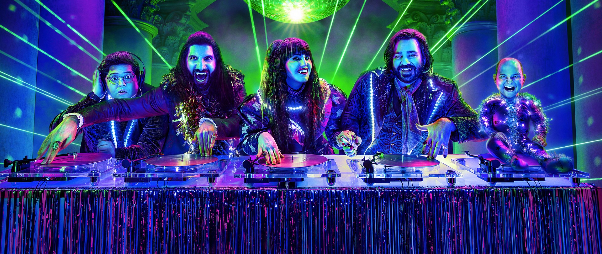 What We Do in the Shadows cast djing on a turn table with green lasers in purple effect