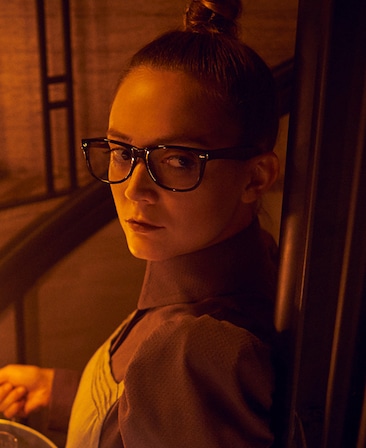 Billie Lourd headshot with hair in bun and glasses looking over shoulder from American Horror Story Apocalypse