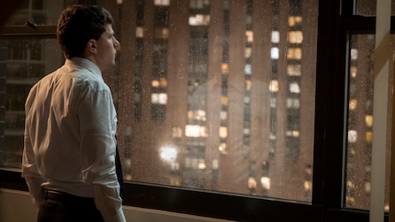 Jesse Eisenberg as Toby Fleishman in white button down staring out window at night with apartment building across in FX's Fleishman Is In Trouble