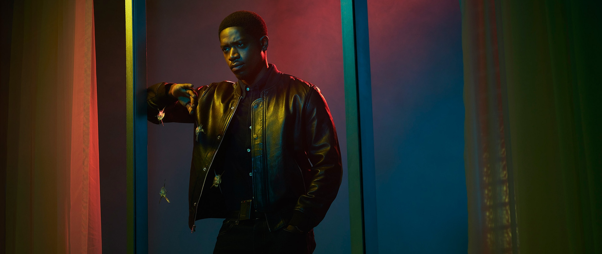 Franklin Saint wearing a leather jacket and leaning against a large window
