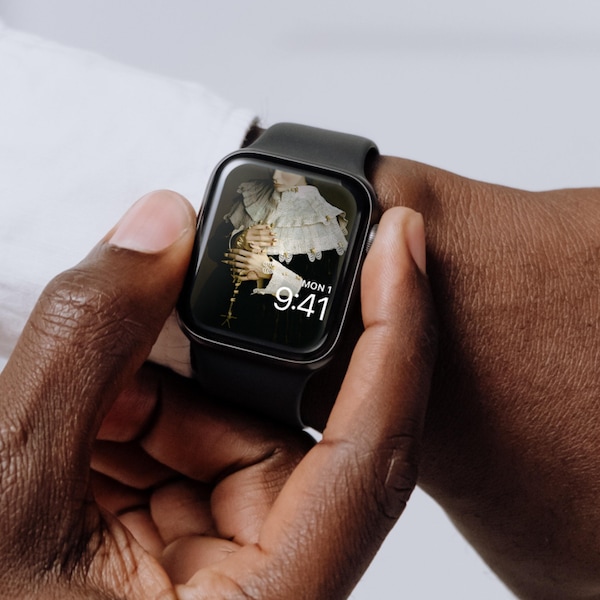 Man holding an Apple Watch with lock screen of a person in pilgrim attire holding a necklace made of human teeth.