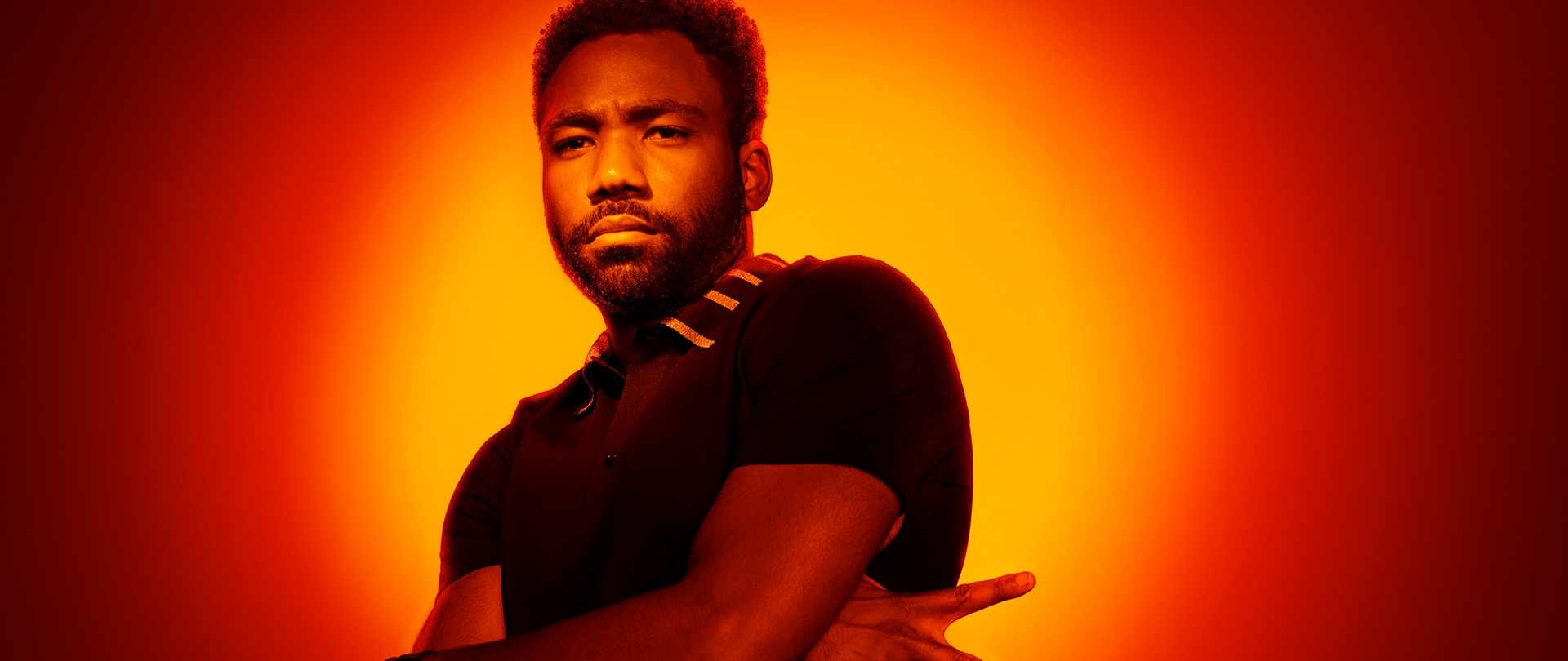 Donald Glover as Earnest Marks in FX's Atlanta with his arms crossed, throwing a peace sign with an orange background.