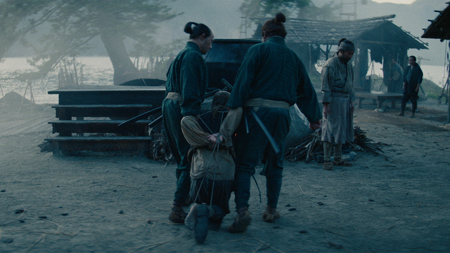 Two samurai carry off Pieterzoon who is bound at his wrists and ankles