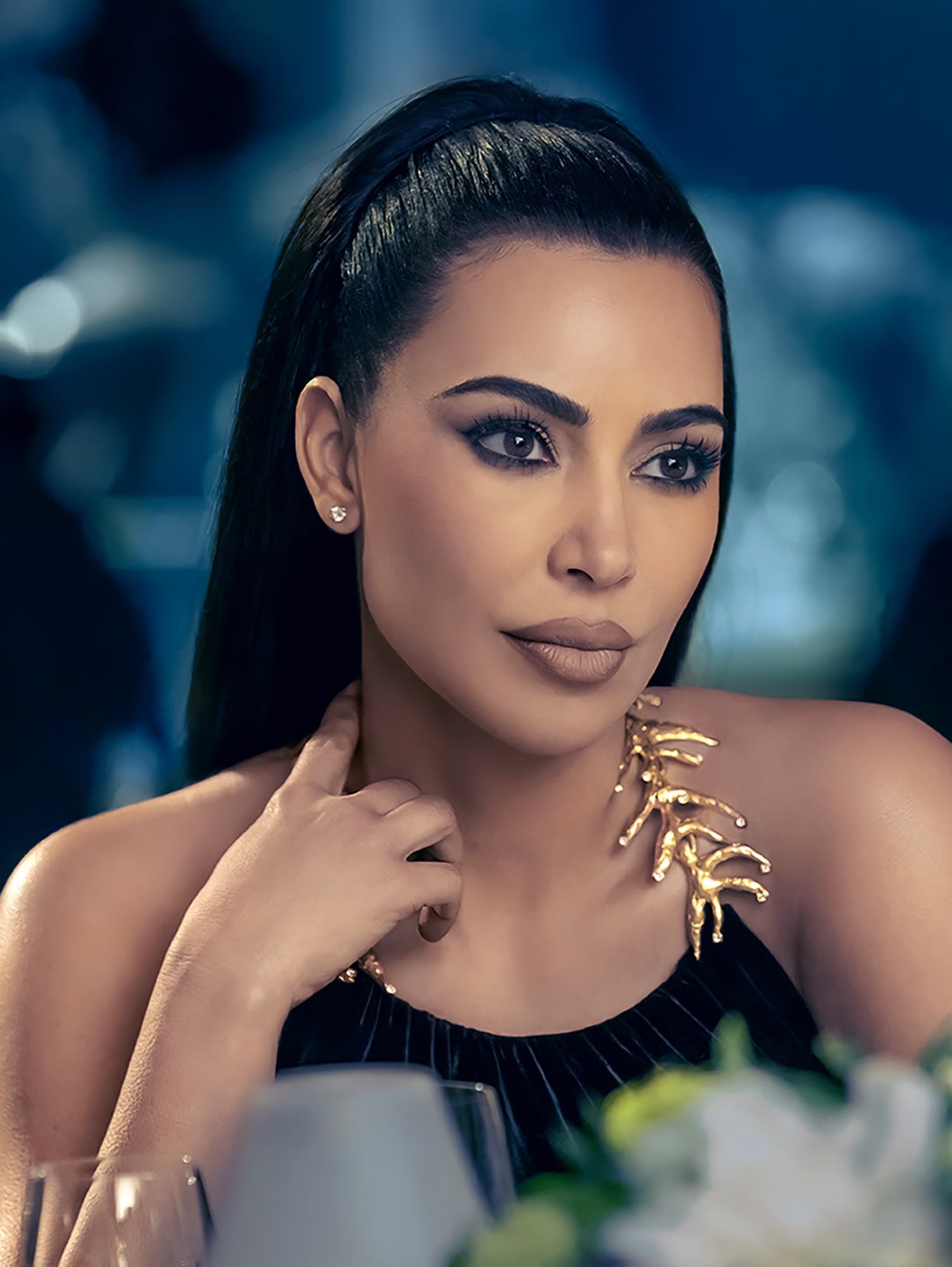 Woman with ponytail wearing a black dress with gold detail. 