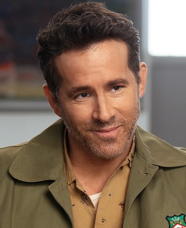 Ryan Reynolds Headshot wearing a green jacket with a Wrexham logo a tan button up underneath