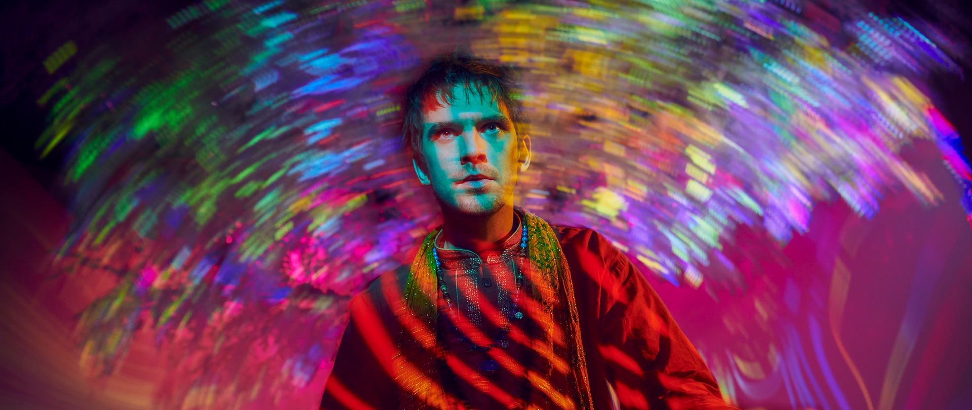 Dan Stevens as David Haller in FX's Legion sitting on the ground with trippy bright colors illuminating the room.