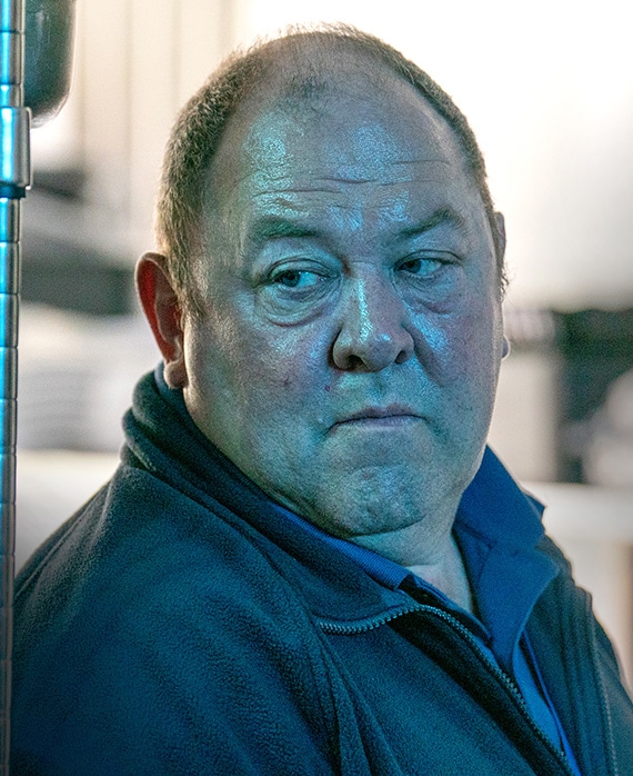 Mark Addy headshot wearing a black zip up jacket and blue shirt