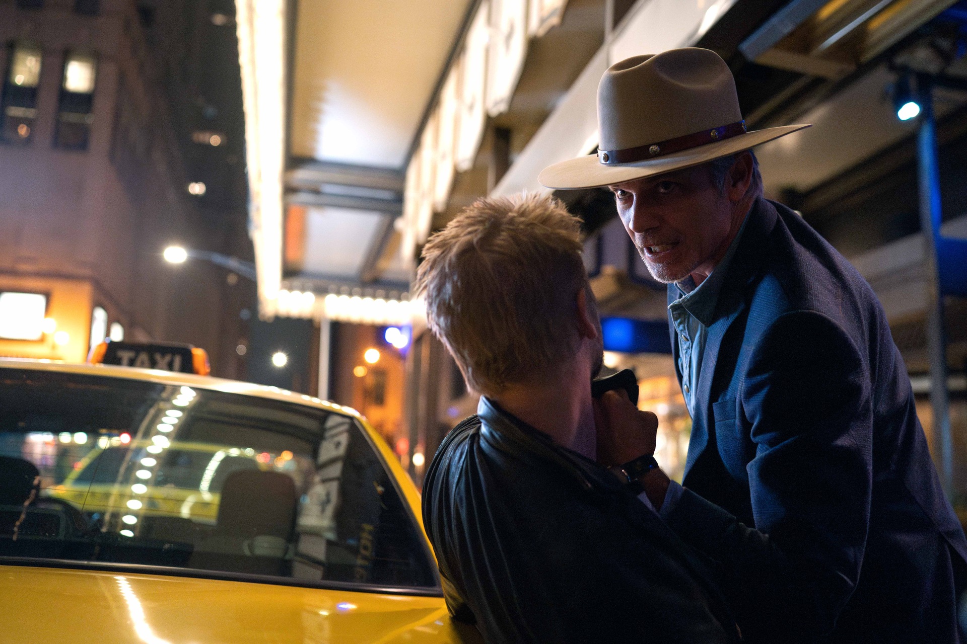 Raylan Givens holding a suspect by the collar against a yellow taxi