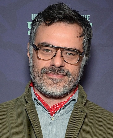 Jemaine Clement headshot wearing glasses with a green jacket.