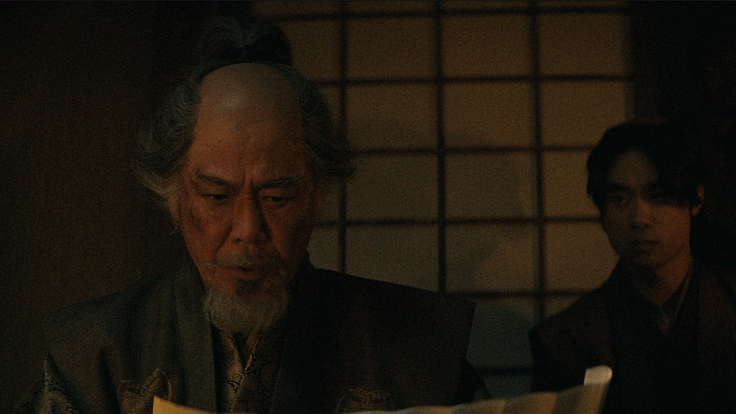 Close up of Hiromatsu in dimly lit room reading a letter