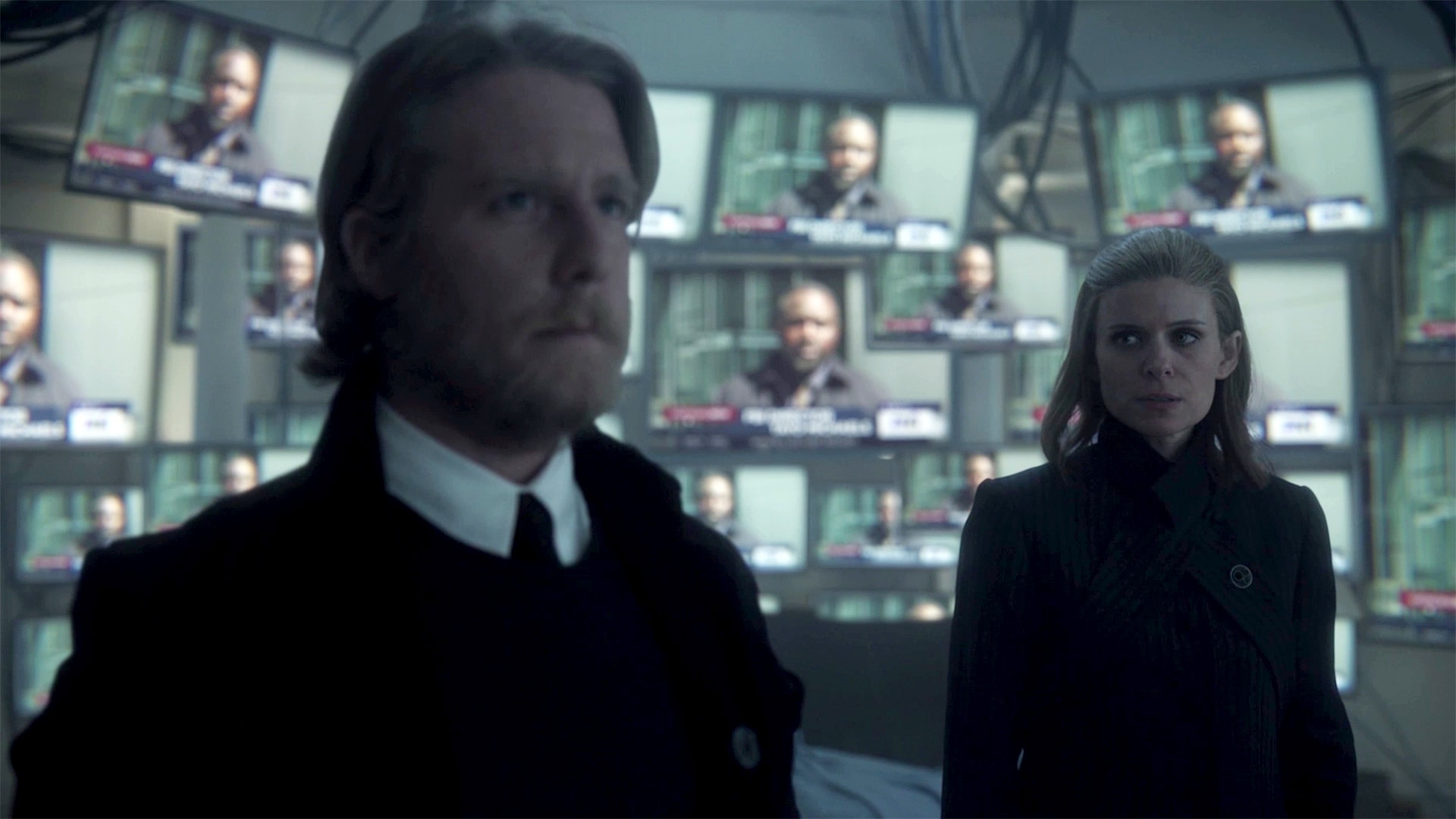 Ashley and Murphy standing in a room with several TV screens
