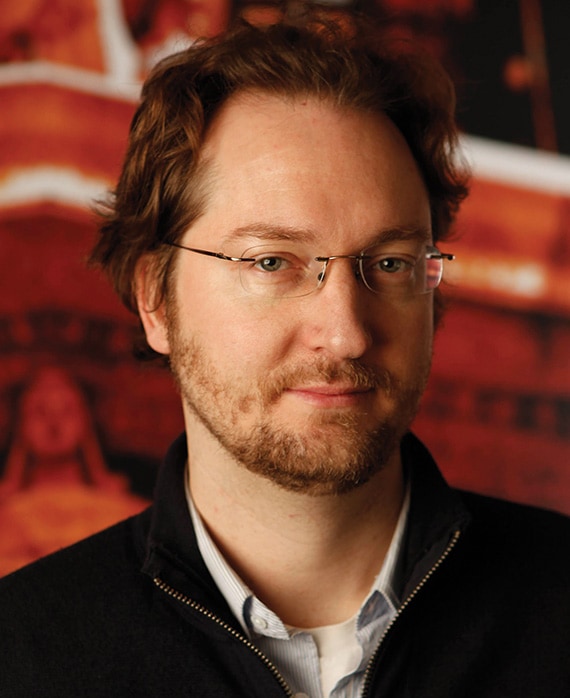 Aaron Zelman headshot in black jacket and blue button down with red and white graphic image of stone sculpture in background
