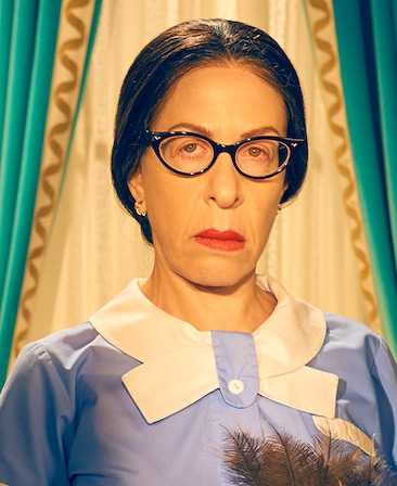 Jackie Hoffman as Mamacita wearing blue and white maid attire in front of teal and gold window drapes in Feud FX show