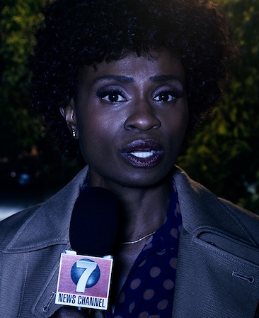 Adina Porter as news anchor in grey coat at night in front of bushes holding News Channel 7 microphone