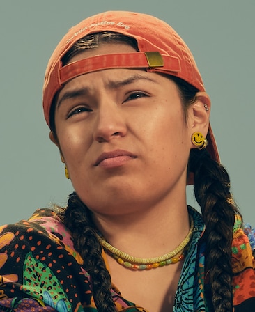 Paulina Alexis headshot wearing a multicolor shirt with a couple beaded necklaces and a backwards orange baseball cap.