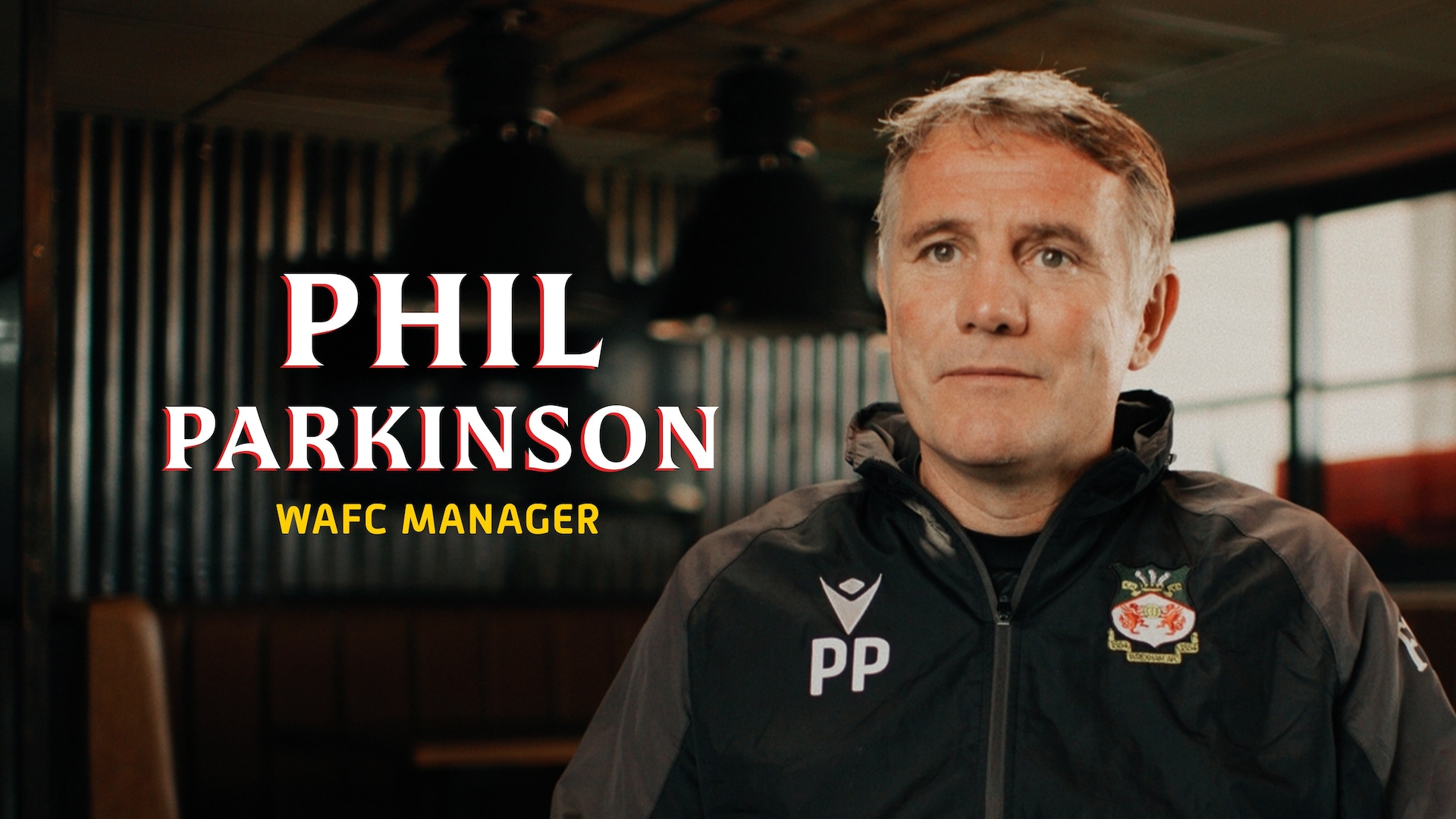 Phil Parkinson headshot wearing a black jacket with a Wrexham logo