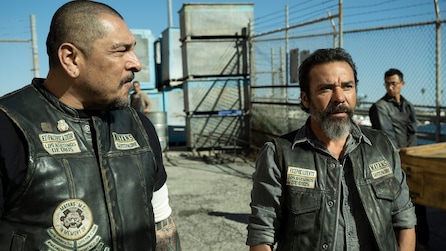 Two men wearing leather biker vests standing outside on a roof