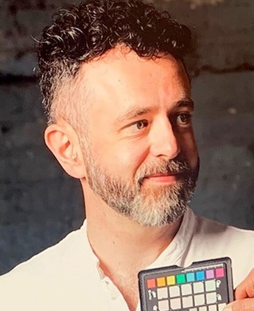 Headshot of Andy Thomas wearing a white button up, looking off to the side with a grey background