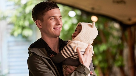 Luke standing outside holding a baby that is wearing a striped hoodie with little ears