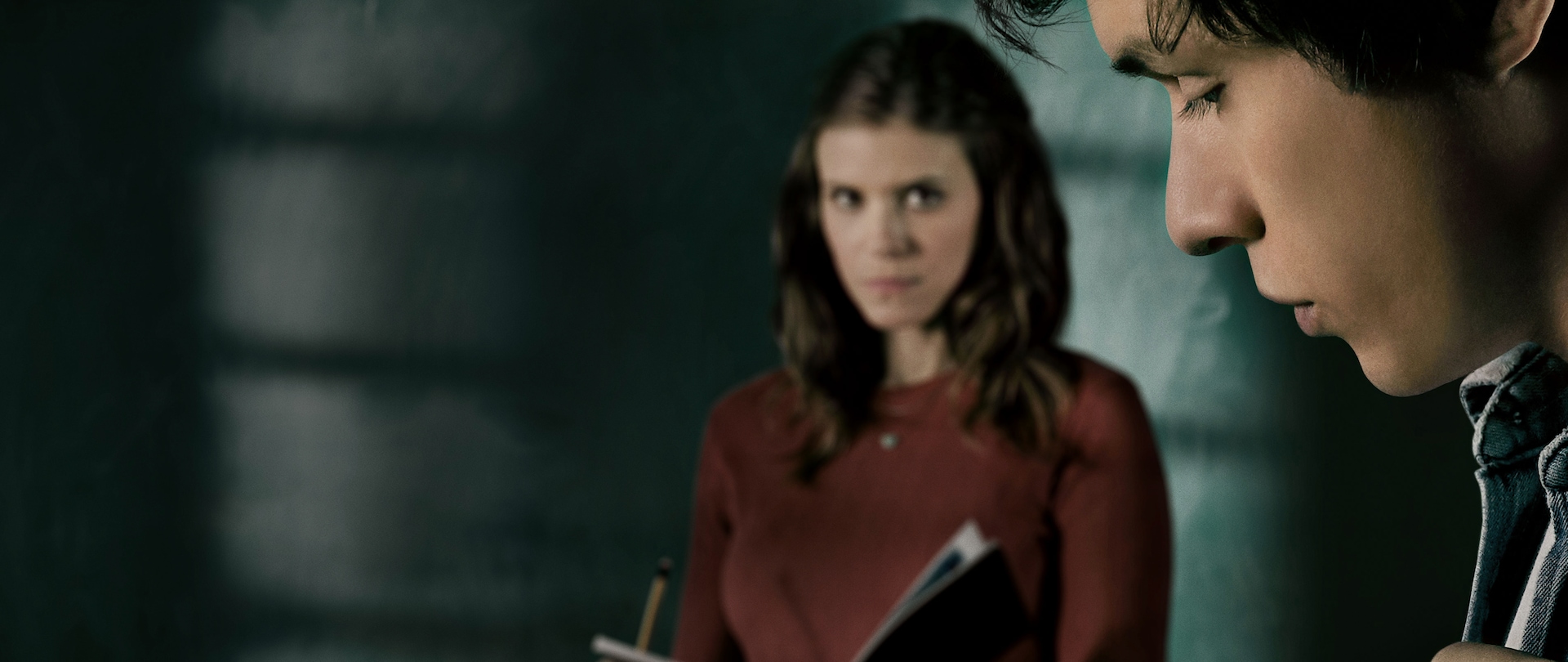 Blurred Kate Mara holding textbook in background standing in classroom with close up of young man's face for FX's A Teacher