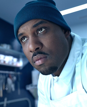 Lionel Boyce headshot wearing blue beanie and white collared shirt and apron.