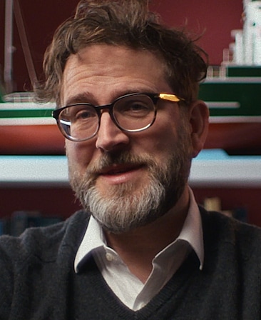 Humphrey Ker headshot wearing a white button up under a grey sweater, wearing tortoise printed glasses.