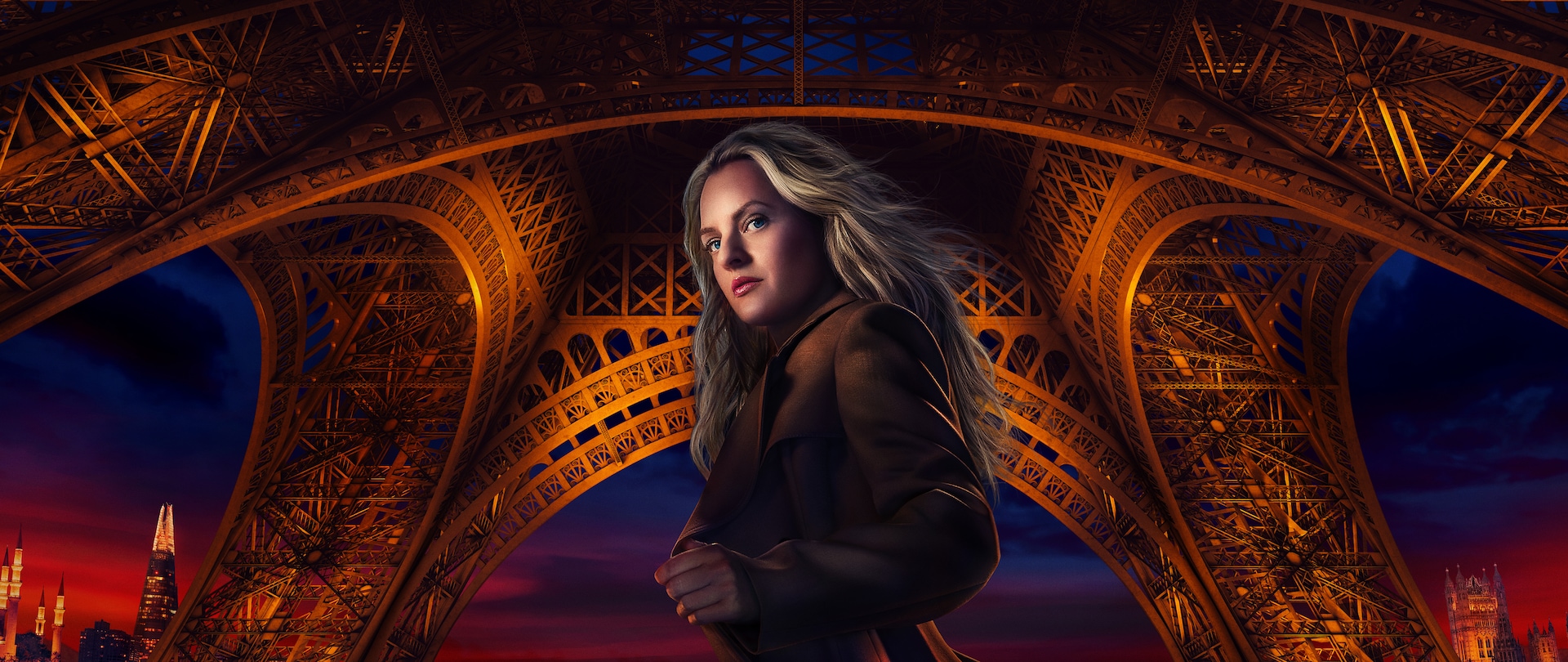 Blonde woman in a brown peacoat standing under the Eiffel Tower that's been lit up at night.