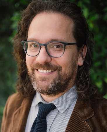 Robert Levine headshot wearing a brown jacket with a navy tie and shirt