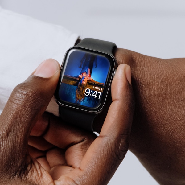 Man wearing Apple Watch with lock screen of woman in red bikini laying down on lake deck with man holding axe behind her
