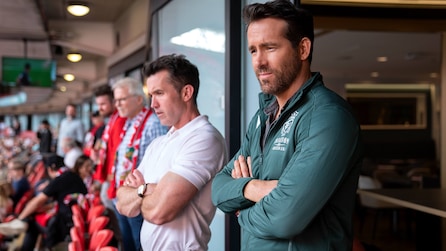 Ryan Reynolds and Rob McElhenney with arms crossed watching a soccer game