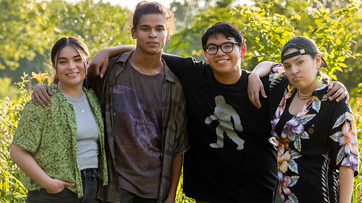 Cast of FX's Reservation Dogs posing for a photo, with green foliage behind them.
