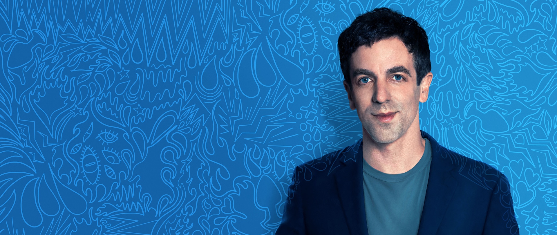 BJ Novak in a sports coat and t-shirt standing in front of a blue colored abstract expression art wall for FX's The Premise