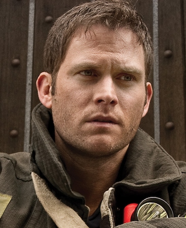 Steven Pasquale headshot wearing a fire jacket and carrying flashlight