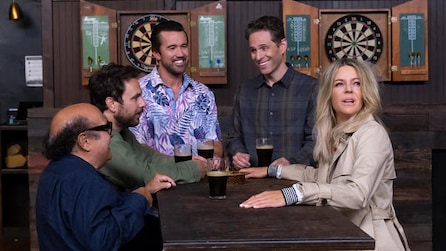 Cast of It's AlwaysSunny sitting at table in bar by dart boards in FX's It's Always Sunny