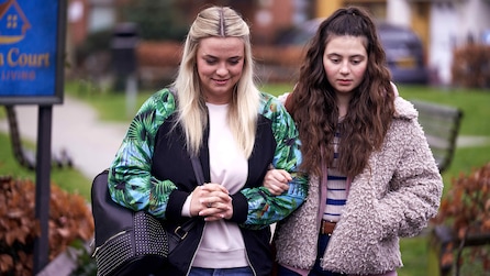 Holly and Ava wearing heavy jackets and walking outside arm and arm