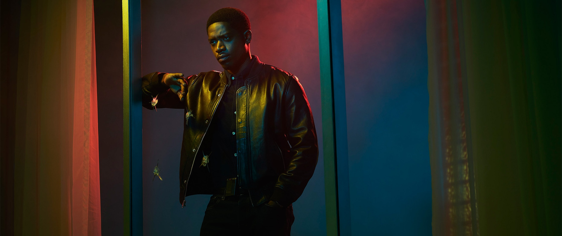 Franklin Saint wearing a leather jacket and leaning against a large window