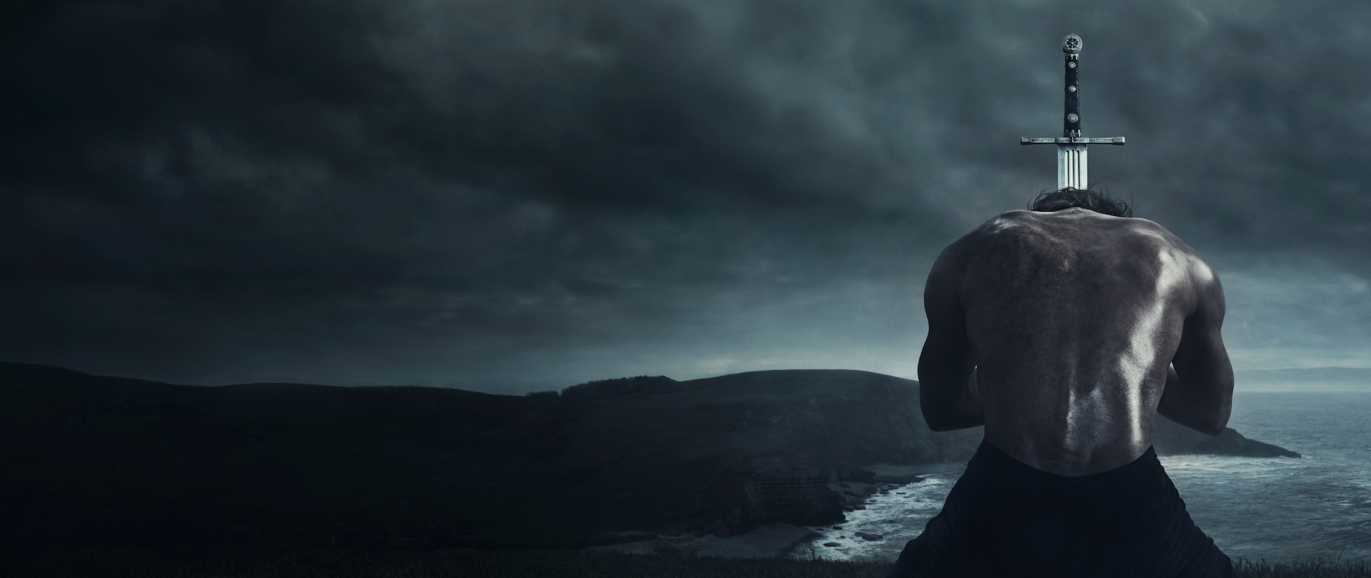Grey skies and coastal landscape with shirtless man kneeling in front of a sword with black hilt for Bastard Executioner