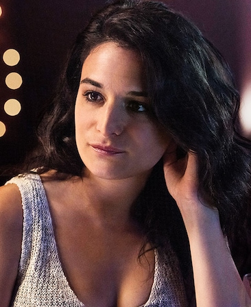 Jenny Slate headshot wearing a white tank top with her hand in her hair