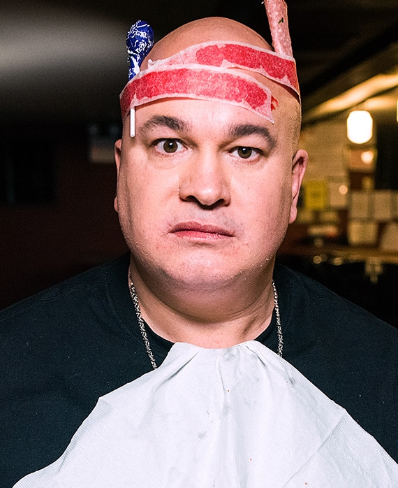 Robert Kelly headshot wearing a black shirt with a white napkin tucked in and red roll up strips around head