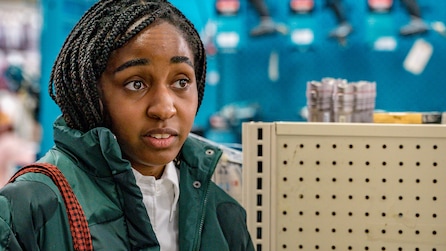Ayo Edebiri as Sydney Adamu wearing green puffer jacket in hardware tool store in FX's The Bear