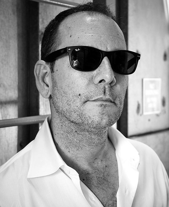 Tim Minear wearing black sunglasses and white button down in black and white headshot 