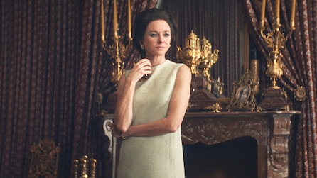 Babe Paley standing in a cream colored dress and holding a cup.
