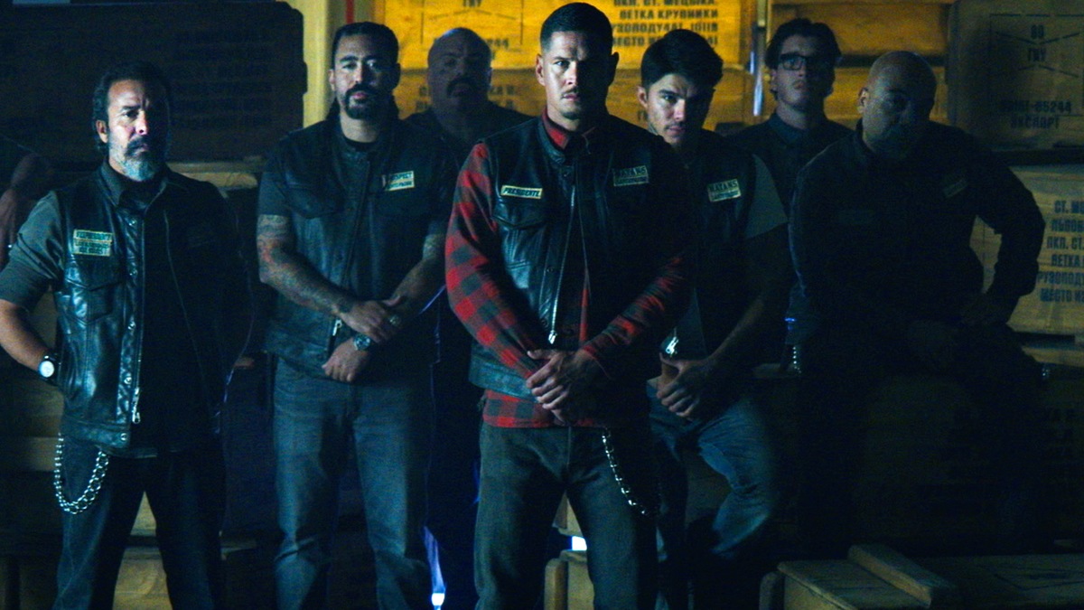 JD Pardo wearing a red flannel shirt crossing his arms, standing in the middle of a group of men in biker gear