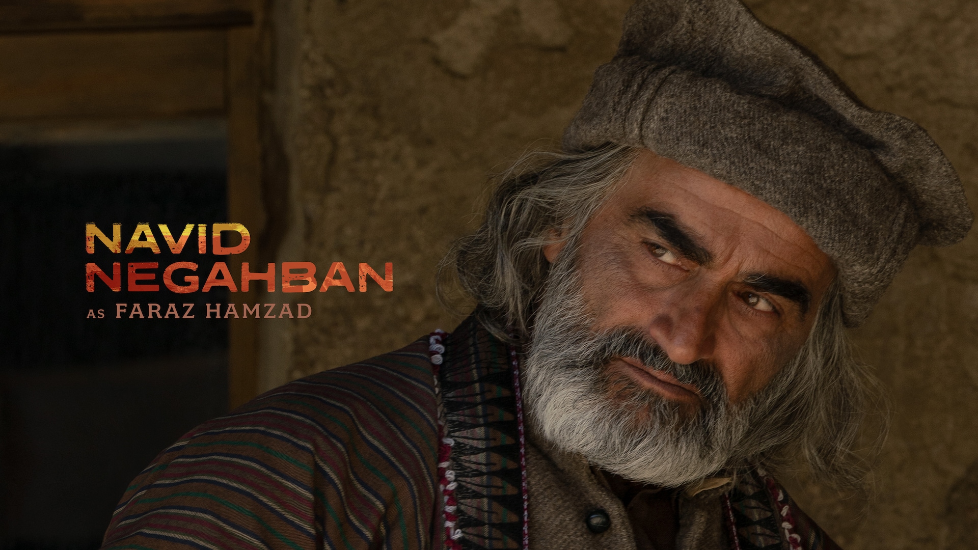 Navid Negahban wearing brown garments against a rocky hill