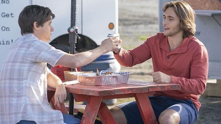 Two boys sitting at a red picnic table shaking hands