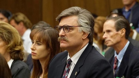 Man with glasses and mustache in black suit sitting in court room in American Crime Story Installment 1 Episode 9