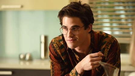 Darren Criss as Andrew Cunanan leaning on arms in kitchen and smiling in American Crime Story Installment 2