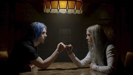 Evan Peters as Kai Anderson and Billie Lourd as Winter Anderson making a promise at a table below a lamp in AHS Cult